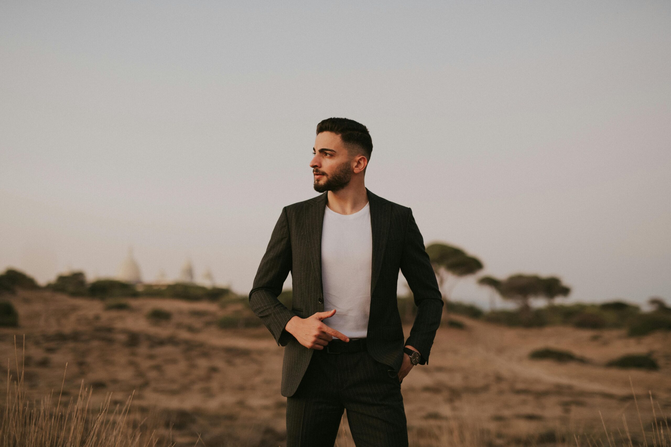 Man in suit posing confidently in a serene desert landscape at dusk.